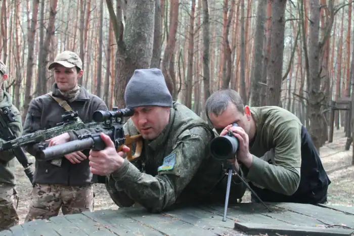 Präzise Schießübung im Wald mit Militärpersonal, Fokus auf Zielgenauigkeit und taktisches Training, in einer natürlichen Umgebung mit Bäumen und Herbstlaub.