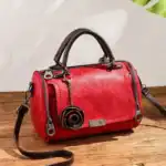 Rote Ledertasche mit schwarzen Griffen und dekorativem Blütenanhänger, stilvoll und praktisch für Damen.